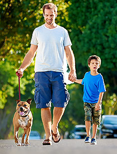Father and son in taking dog for a walk on suburb street